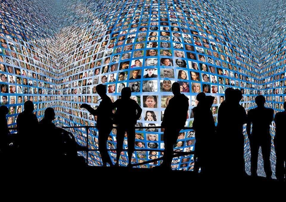 Silhouetted people stand before a huge curved wall of faces on screens, a picture of always-connected Gen Z