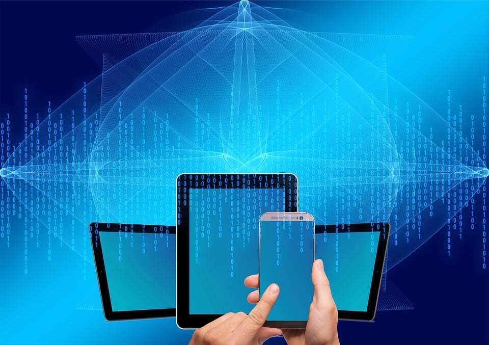 A hand holds a smartphone in front of tablets and glowing digital code, the devices Gen Z students use